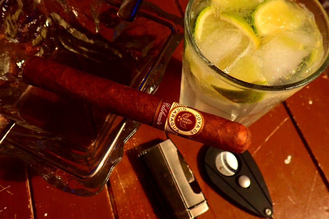 Zigarre im Aschenbecher und Cocktail im Hintergrund